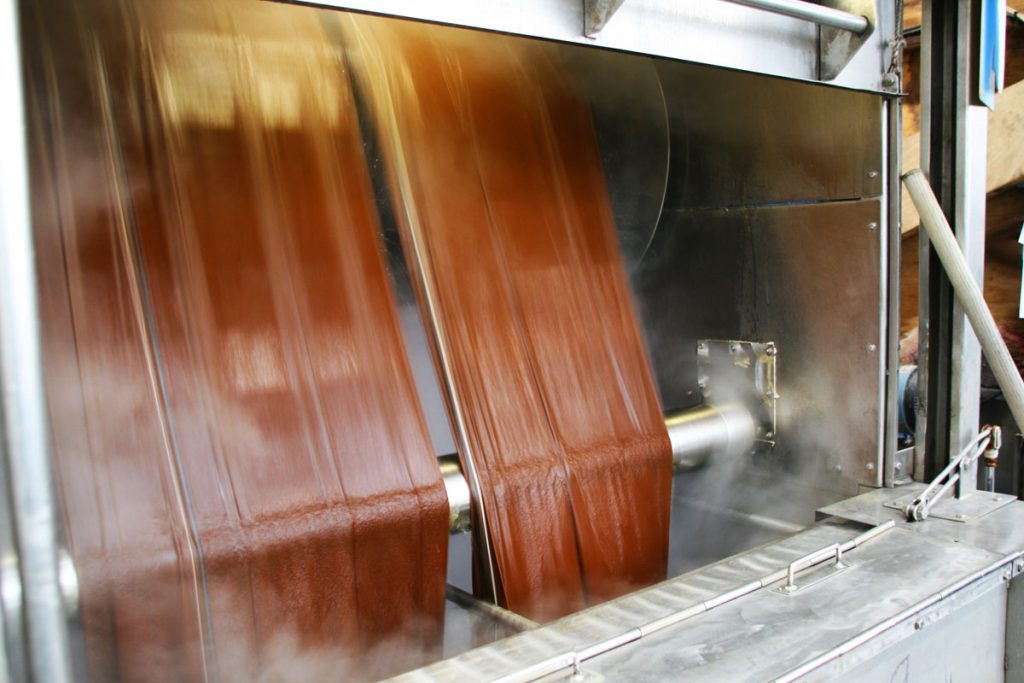 Rust-coloured cloth passing through a steaming finishing machine