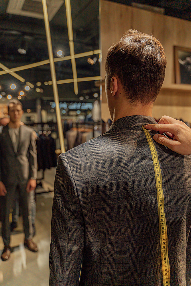 Tailor measuring a customer's jacket shoulder during a bespoke suit fitting