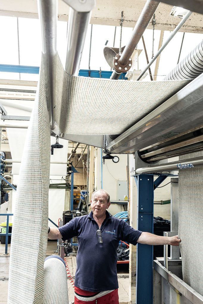 Man inspecting pale grey houndstooth check cloth panels hanging from an overhead finishing conveyor