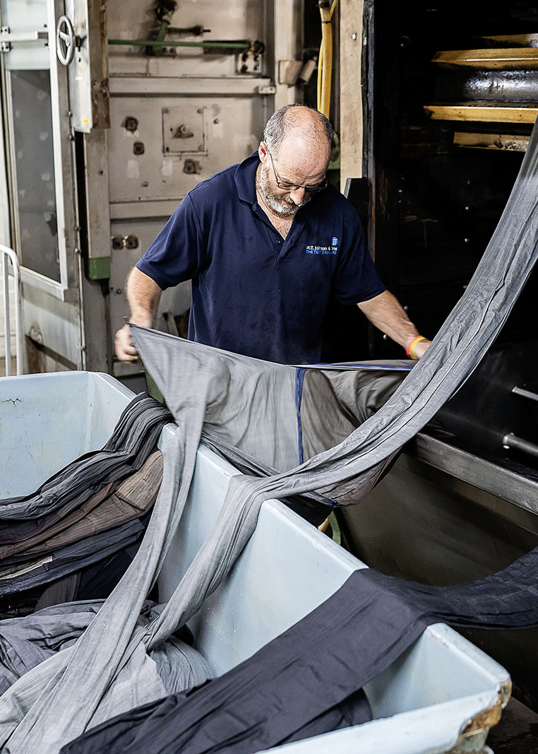 Worker pulling finished grey cloth from a finishing machine into a collection bin