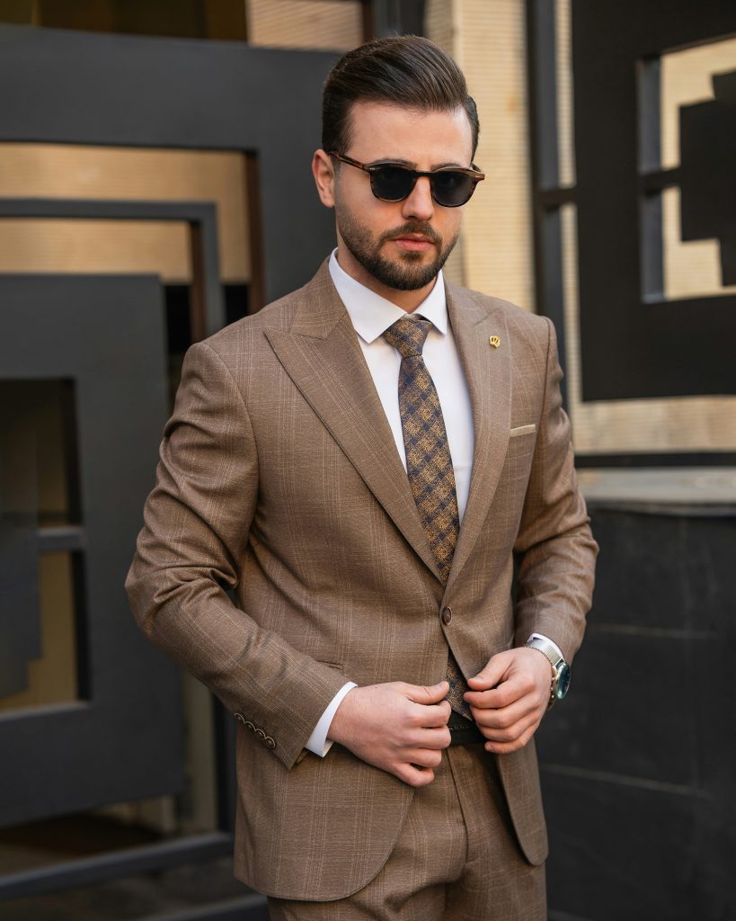 Man wearing a tailored brown check suit and sunglasses standing outdoors