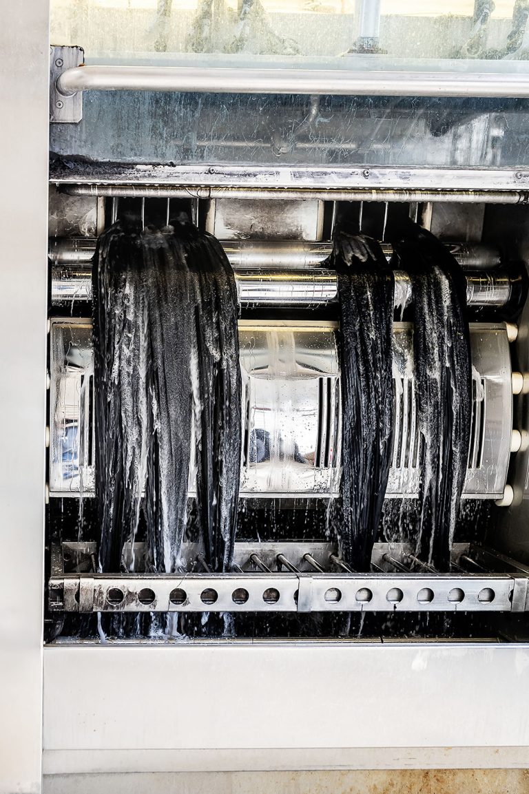 Wet navy cloth strands passing through the scouring machine's wash rollers