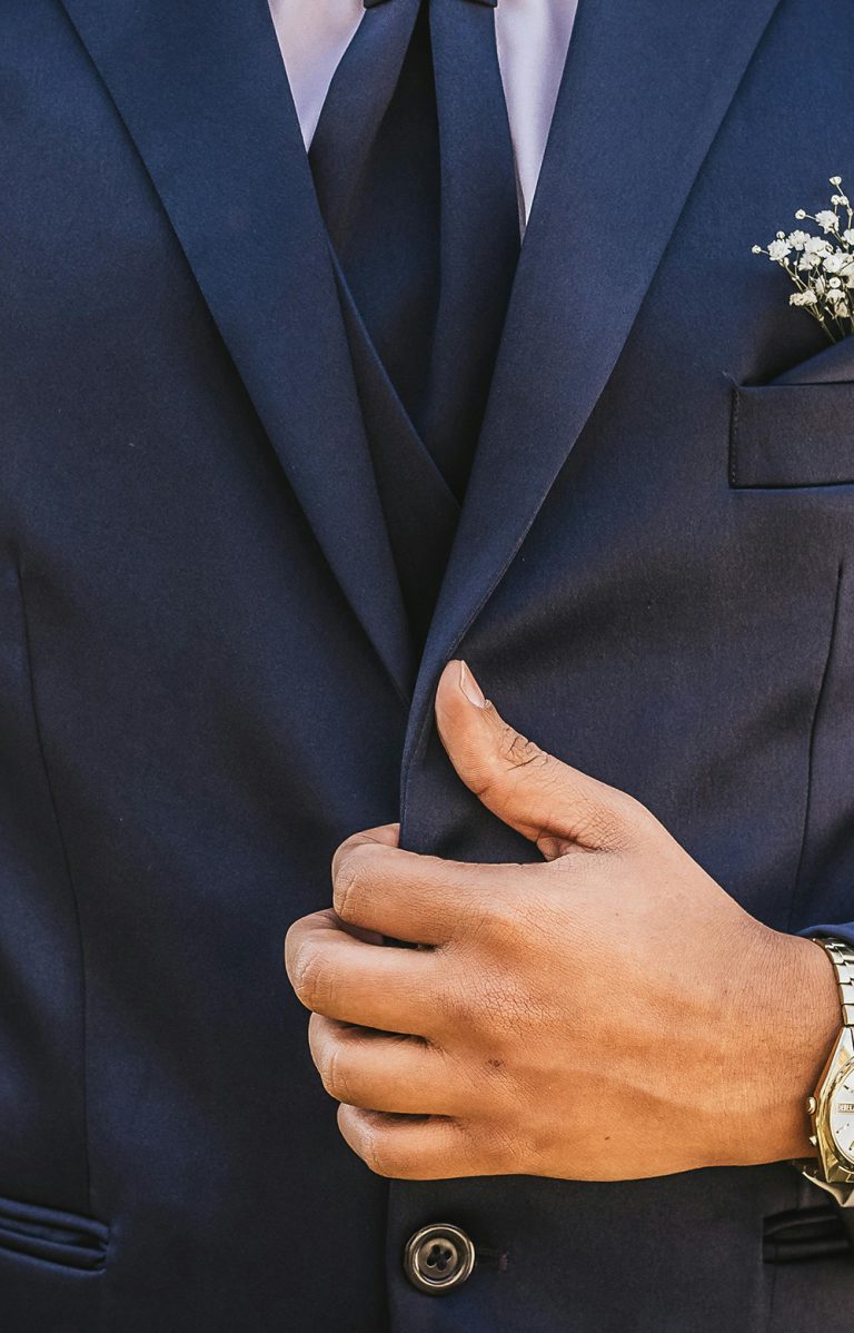 Close-up of a man adjusting the lapel of a navy tailored suit jacket with a boutonniere