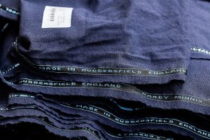 Close-up of stacked navy wool cloth with 'Made in Huddersfield England' selvedge