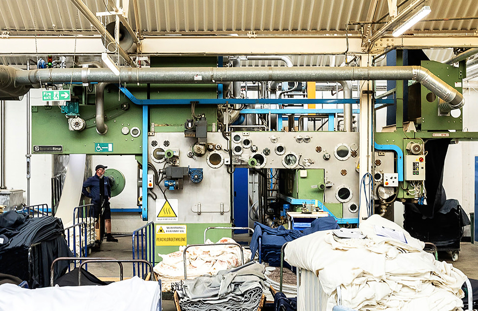Wide view of the scouring plant floor with machinery and stacked cloth trolleys