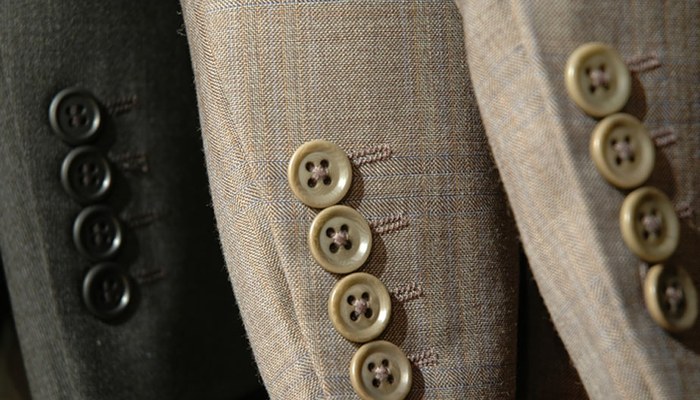 Close-up of jacket lapel buttons on three different wool cloth swatches