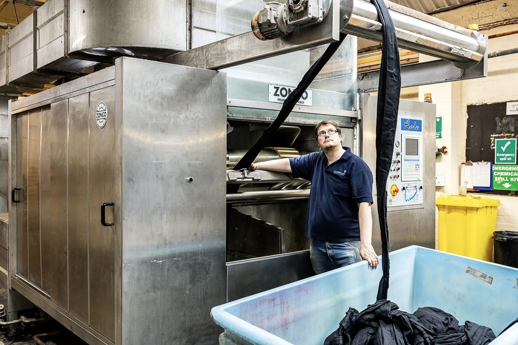 Team member operating the Zonco scouring machine with cloth feeding into a bin