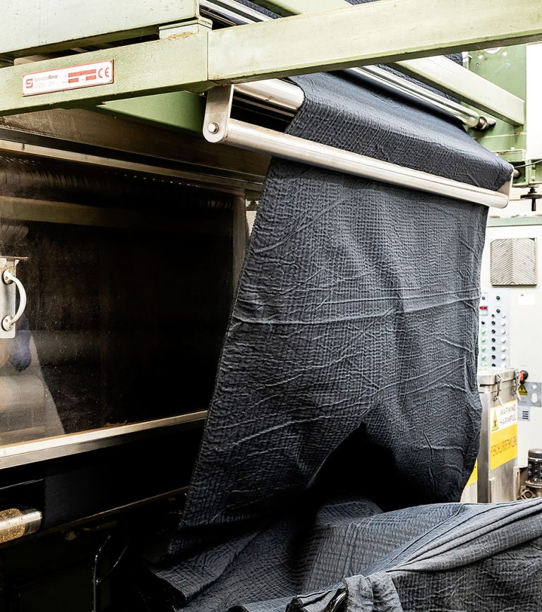 Crinkled dark wool cloth hanging from the rack of the scouring machine