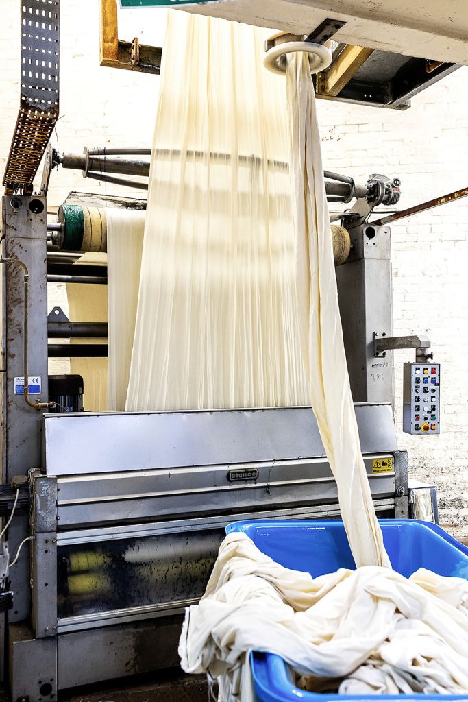 Raw wool cloth passing through scouring machine rollers into a collection tub